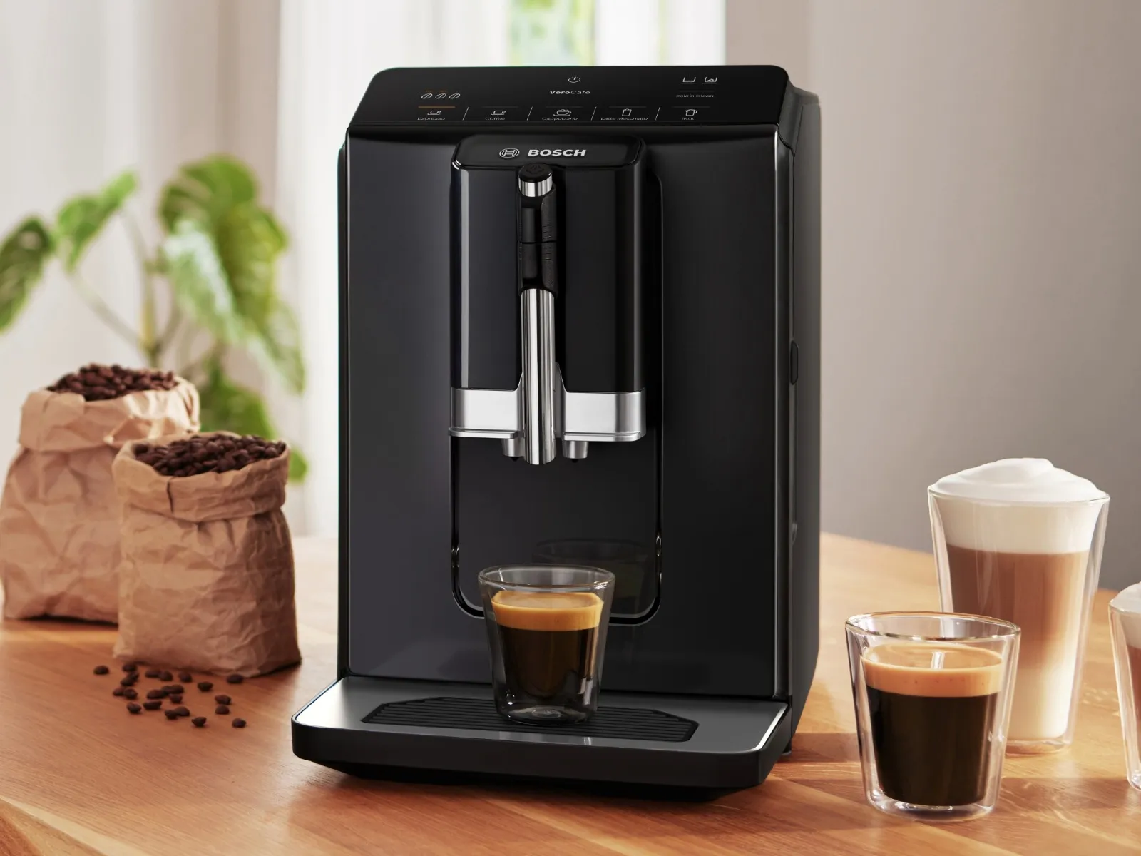 Μηχανή Espresso Bosch Σειρά 2 στέκεται πάνω σε ένα τραπέζι, περιτριγυρισμένη από ροφήματα όπως ένας εσπρέσο και latte macchiato.
