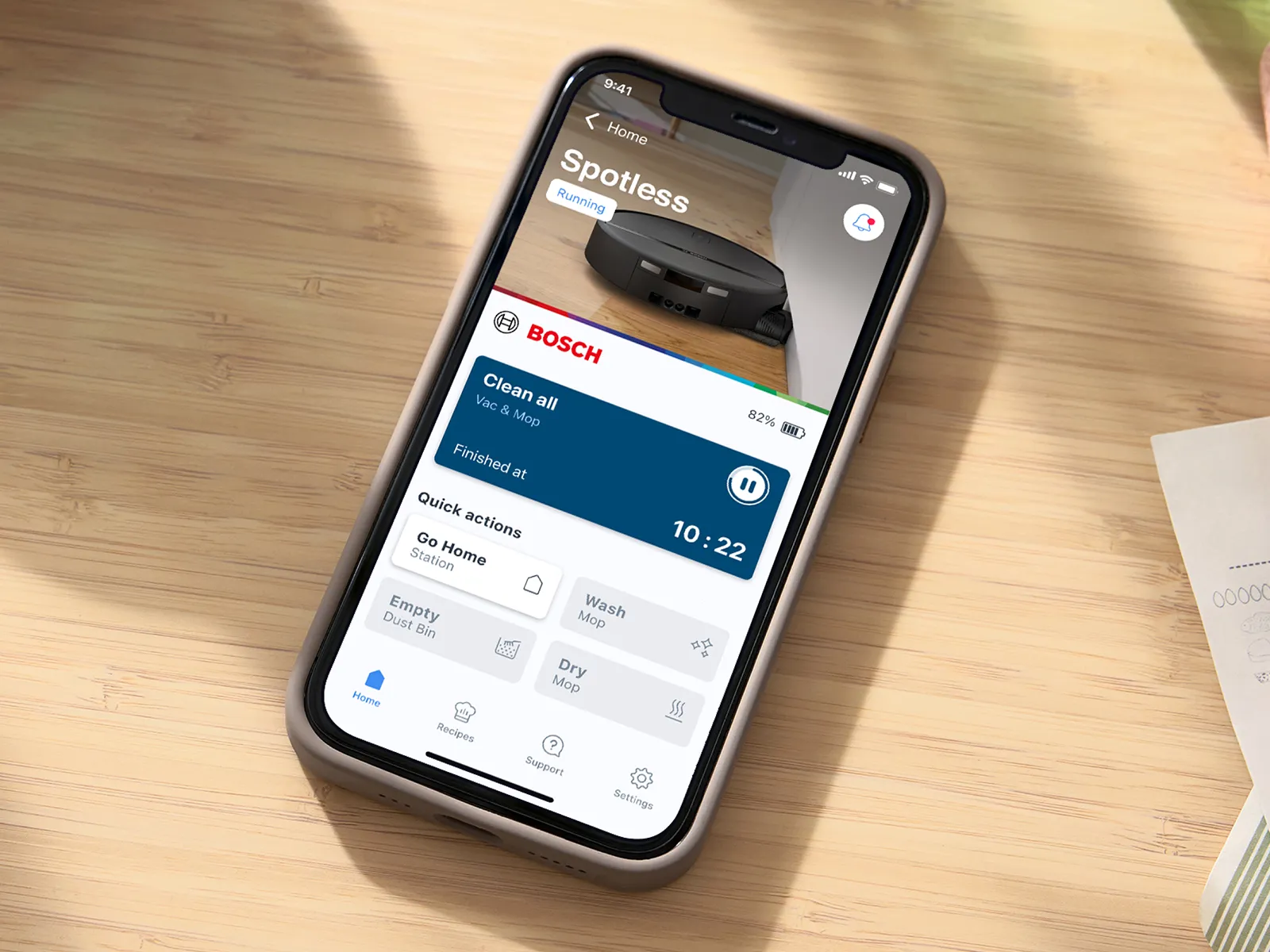 A smartphone displays the Bosch Home Connect app, used to control the cleaning settings of the Spotless 2.