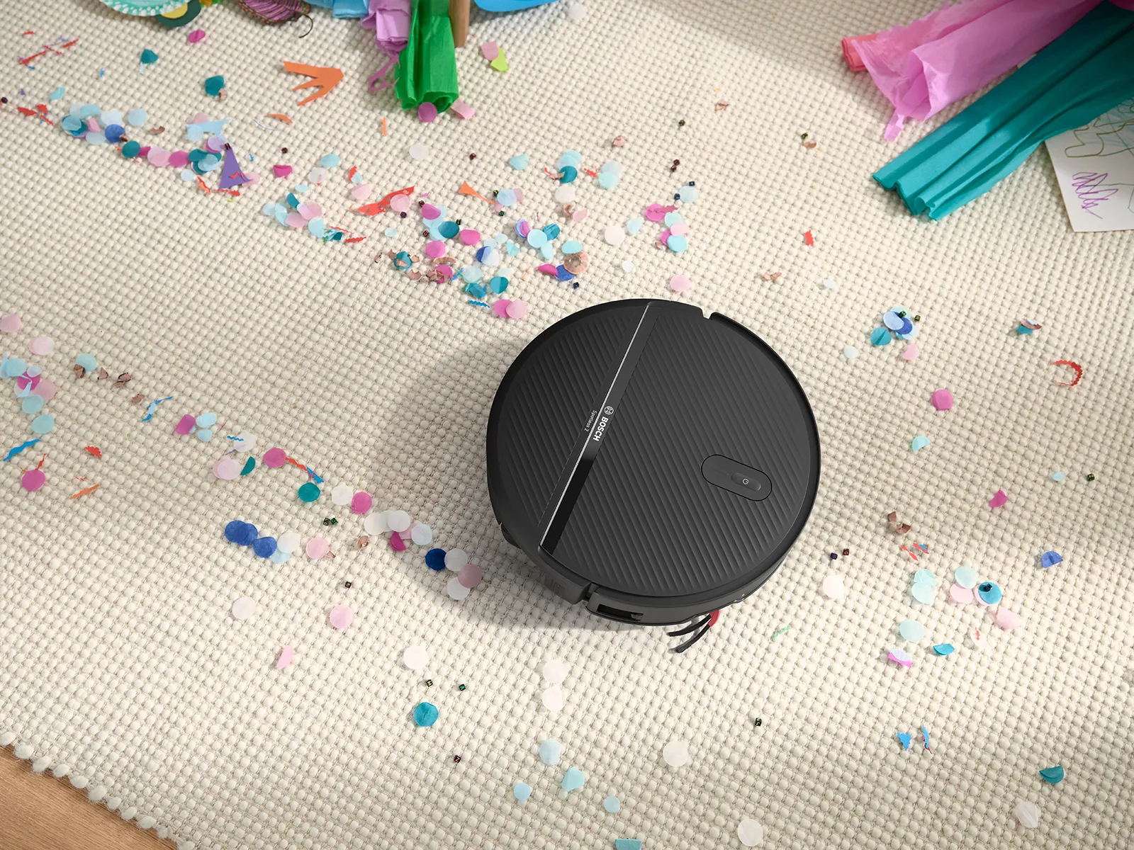 Spotless 2 on a white carpet, clearing a path through confetti, showcasing its suction power.