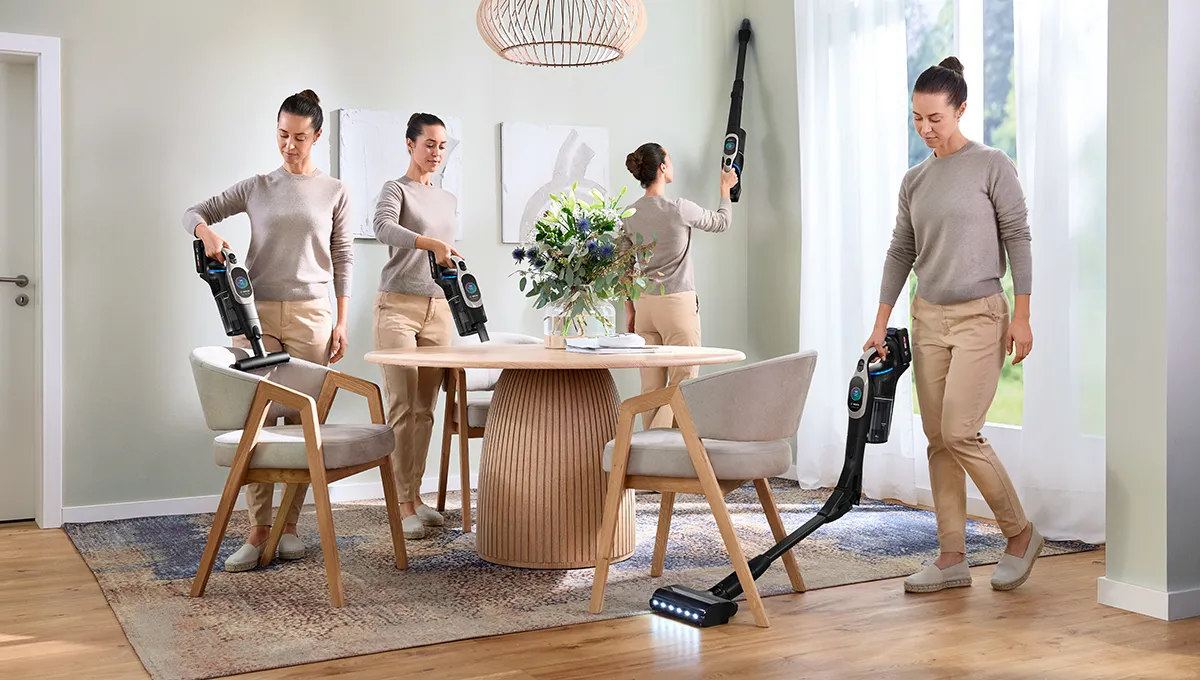 Woman uses Unlimited 10 stick vacuum in a dining area: cleaning upholstery, table, high wall with extension, and under table with flexible joint, showing adaptability
