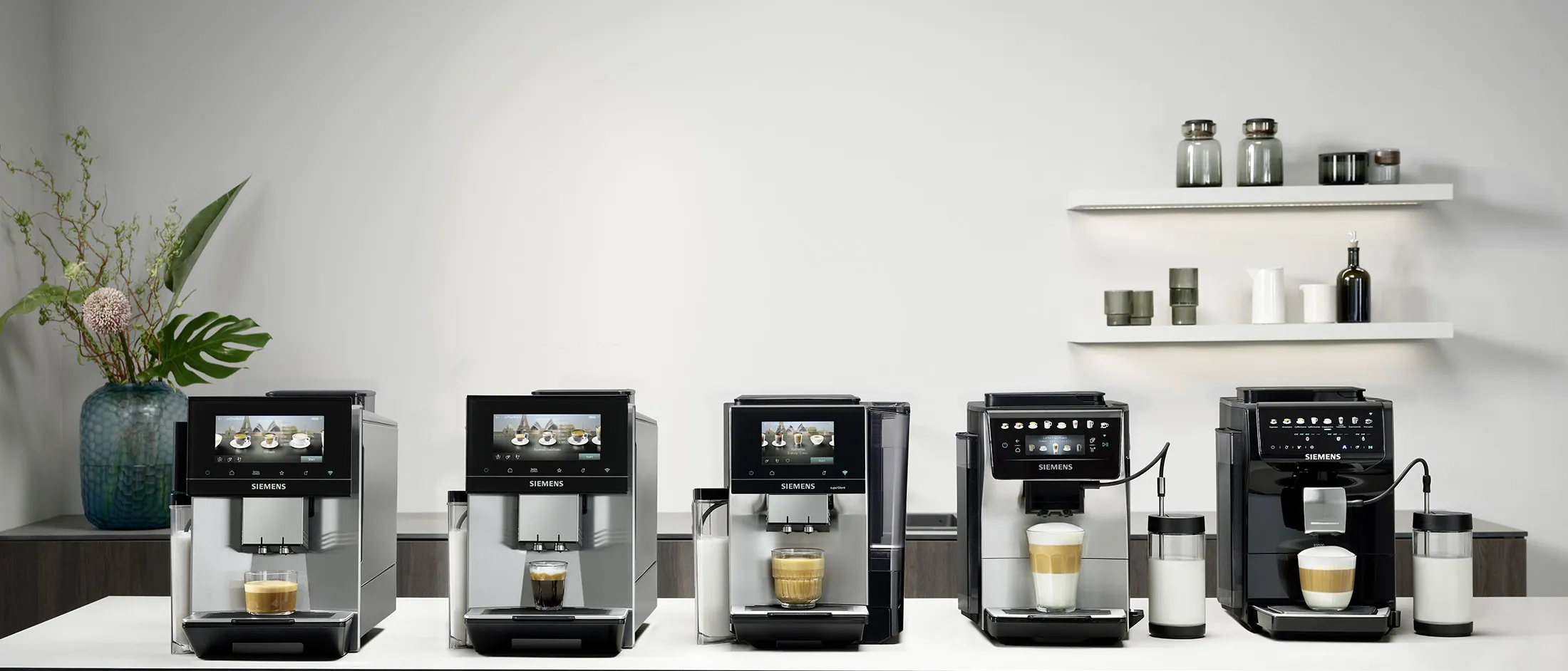 Cinq machines à café automatiques alignées sur un plan de travail, préparant différentes boissons, décor minimal avec un vase et des étagères murales.