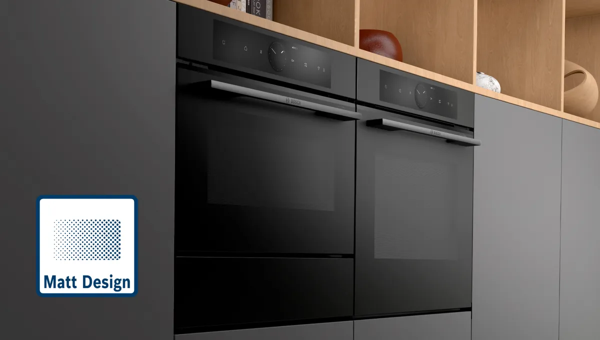 Matte schwarze Doppel-Einbaubacköfen in einer modernen Küche mit dunklen Schränken und offenen Holzregalen darüber.