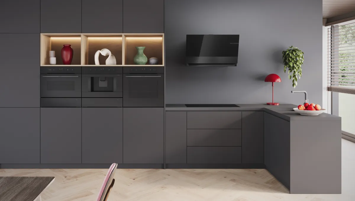 Moderne Küche mit mattgrauen Schränken, Einbaubackofen, offenen Regalen mit dekorativen Vasen, Wand-TV und eine rote Lampe durch ein Fenster.
