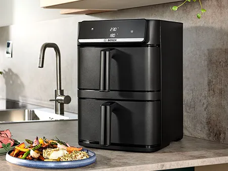 The Bosch Series 6 Double Stack Drawer stands on a kitchen counter with dishes of food around it.