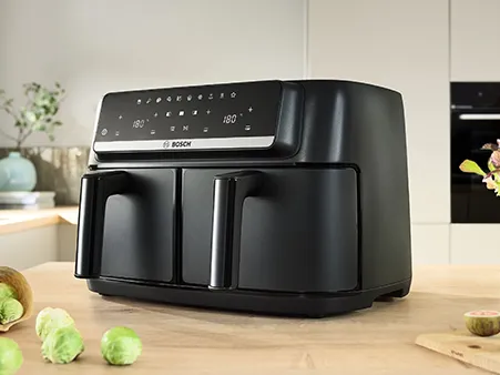 The Bosch Series 4 Double Drawer Air Fryer sits on a kitchen counter with vegetables.