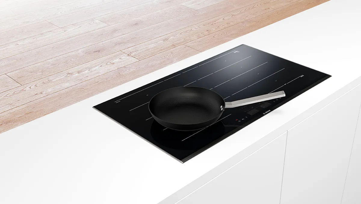 Sartén negra en una moderna encimera de inducción con una encimera de cocina blanca en el fondo.