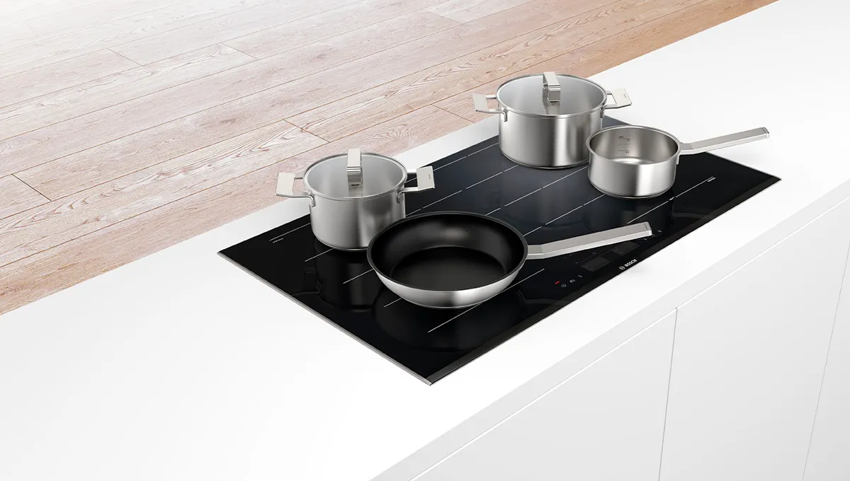 Utensilios de cocina de acero inoxidable sobre una encimera de inducción negra en una cocina moderna.