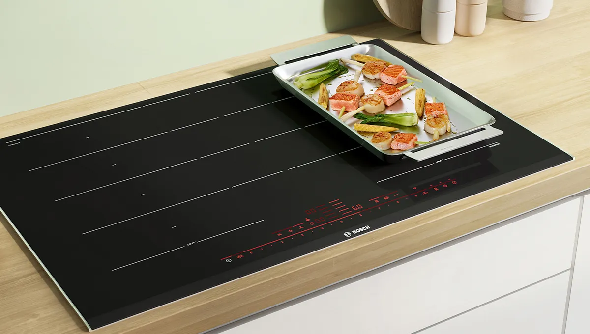 Encimera de inducción con bandeja de comida, electrodomésticos de cocina y planta en maceta sobre encimera de madera.