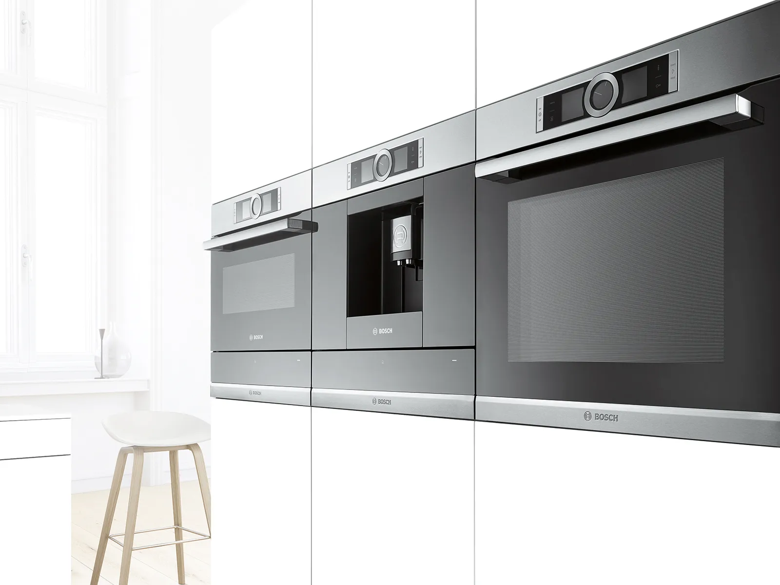 Cocina moderna con microondas, cafetera y horno empotrados Bosch, integrados en elegantes muebles blancos junto a un taburete de madera.