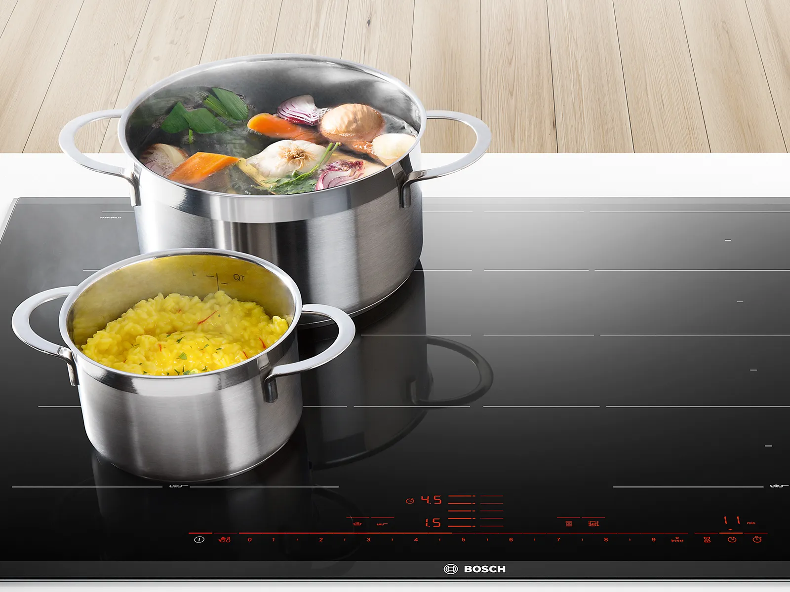 Ollas de acero inoxidable sobre una placa de inducción negra, una con verduras y la otra con arroz cocido.