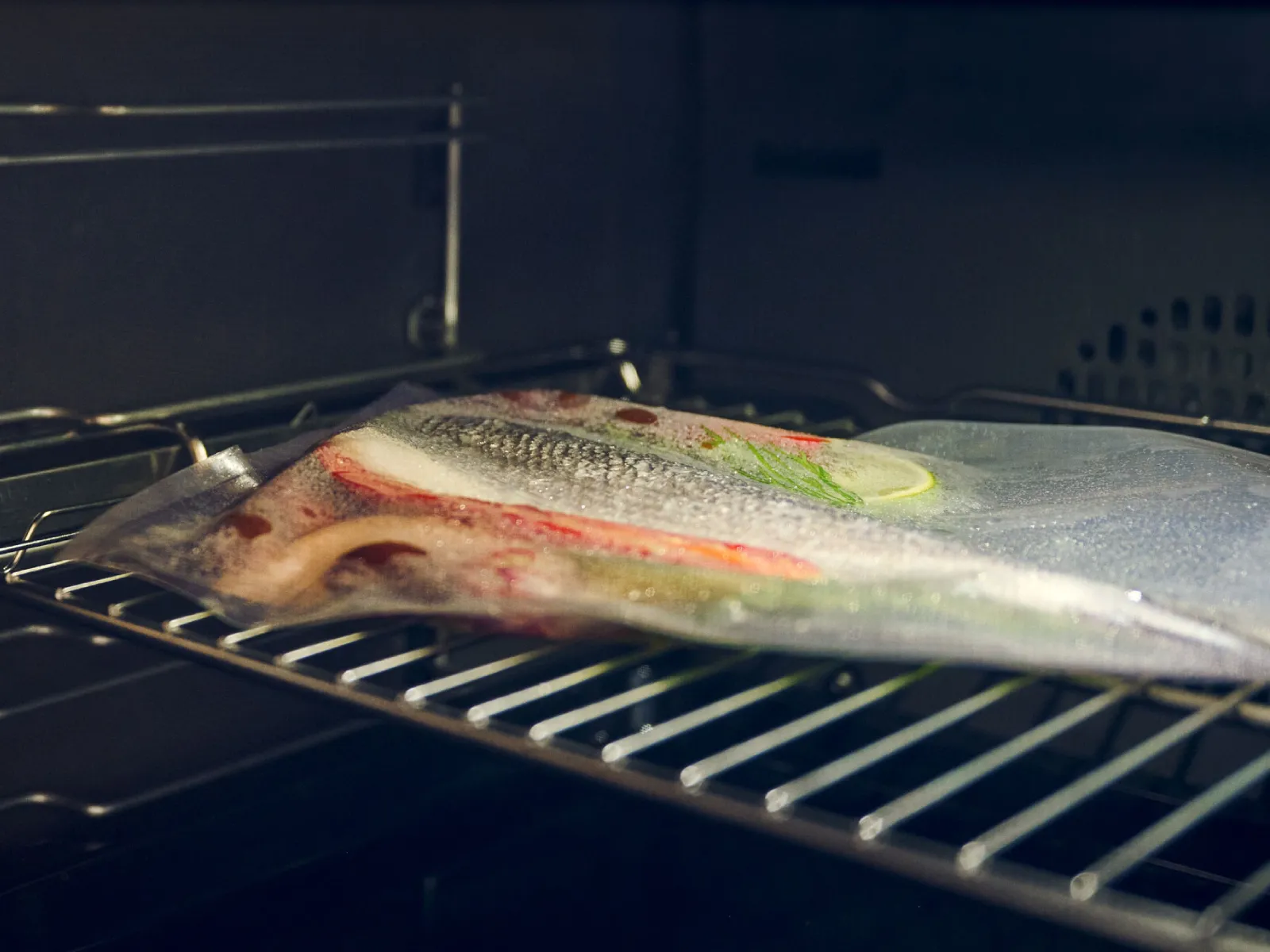 Pesce crudo con limone ed erbe aromatiche sigillato in un sacchetto sottovuoto all'interno di un forno su una griglia di metallo, cottura in stile sous vide.