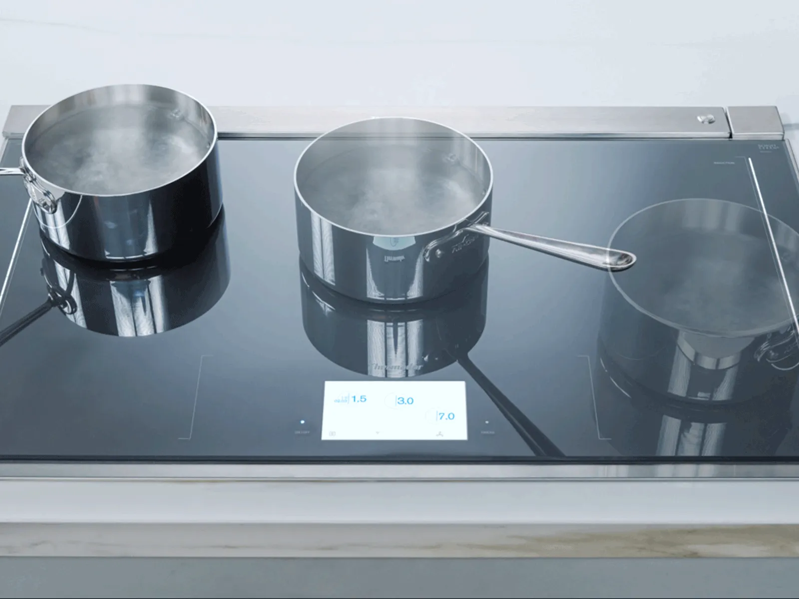 Thermador Induction cooktop with three pots of boiling water on glass surface showing a digital display.
