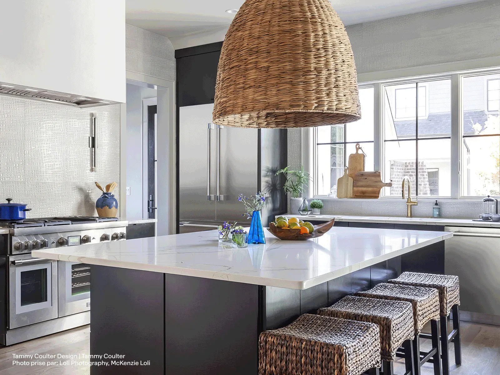 Modern kitchen with large island, wicker stools, and pendant light, featuring Thermador stainless appliances.