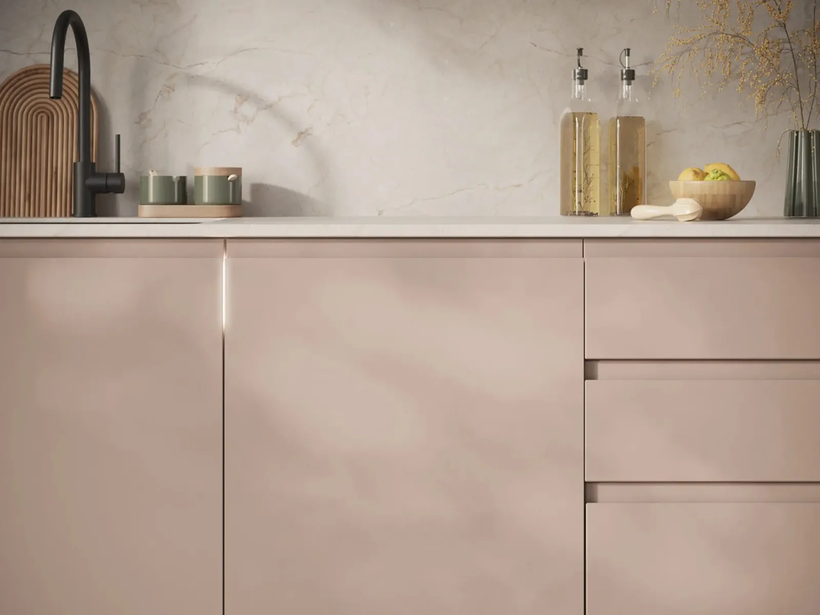 Minimalistische Küchenarbeitsplatte mit rosafarbenen Schränken, einem schwarzen Wasserhahn, Schneidebrettern, Glasflaschen und einer Schale mit Zitronen.