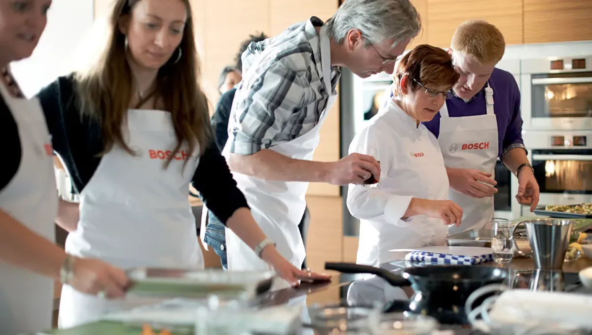 Trzy osoby przygotowujące jedzenie razem w kuchni, siekanie warzyw i za pomocą przyborów kuchennych.