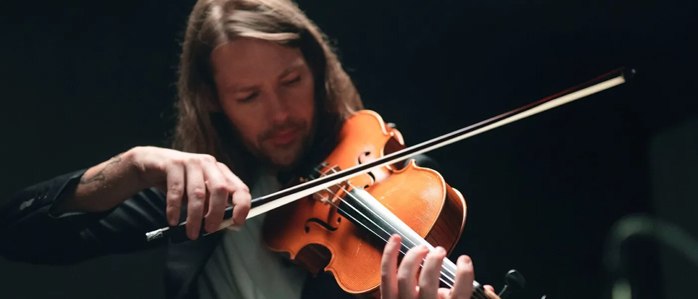 Uomo con i capelli lunghi che suona un violino.
