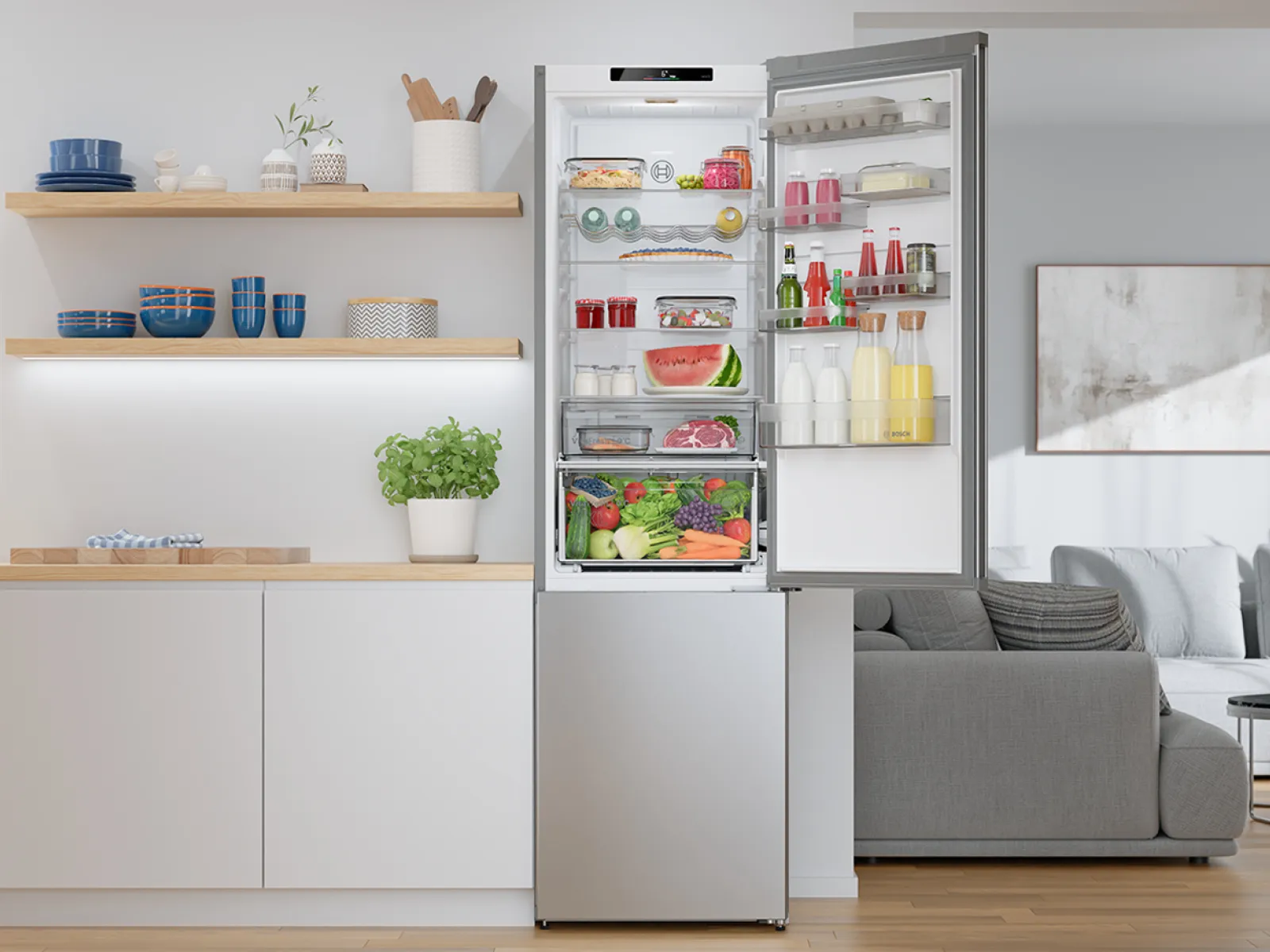 Moderne koelkast met open deur in een keuken met wandplanken en een grijze bank in de aangrenzende woonkamer