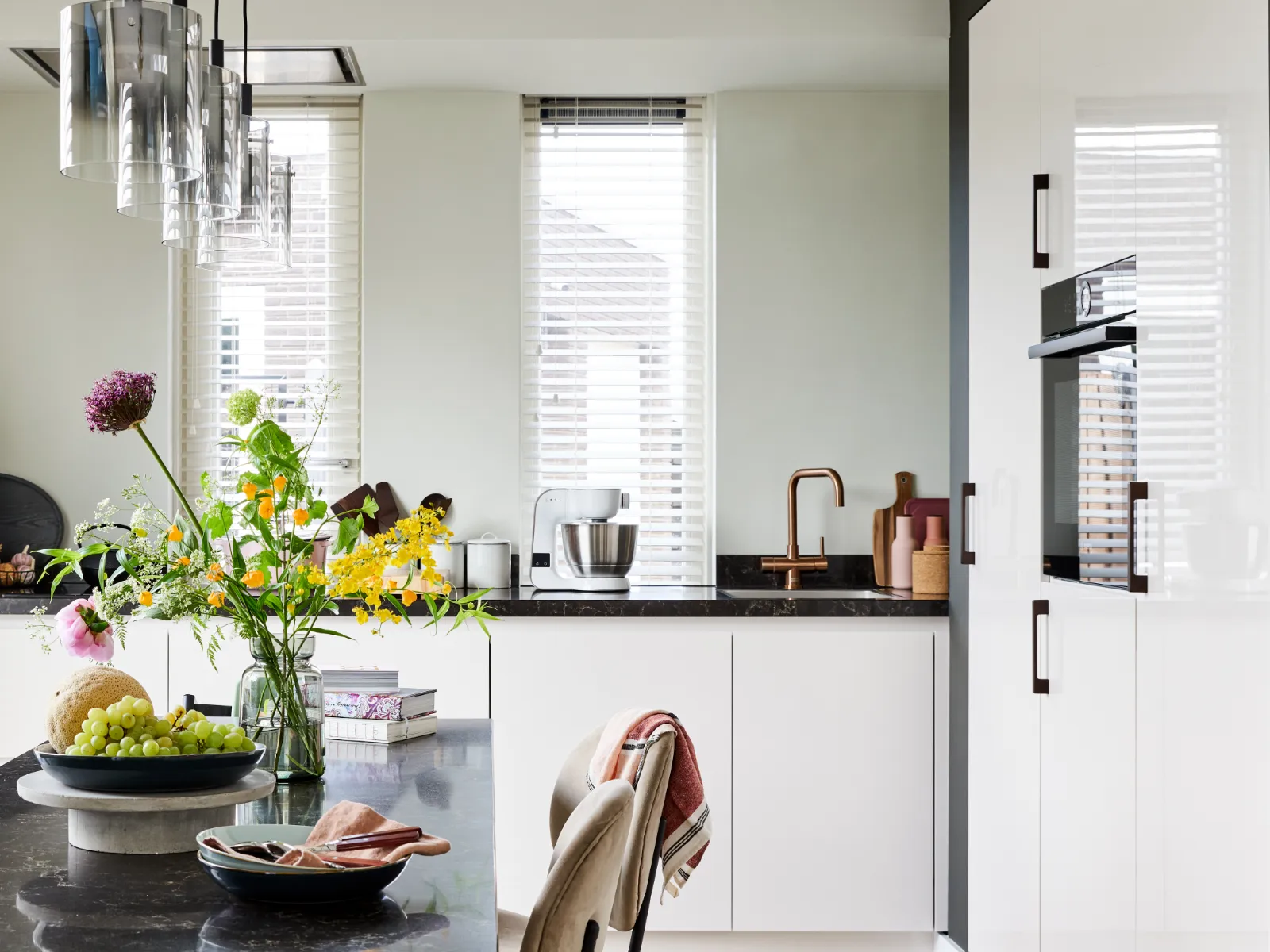 Cuisine moderne avec armoires blanches élégantes, comptoirs noirs, lampes pendentif, et un coin repas avec une table et des chaises en bois.