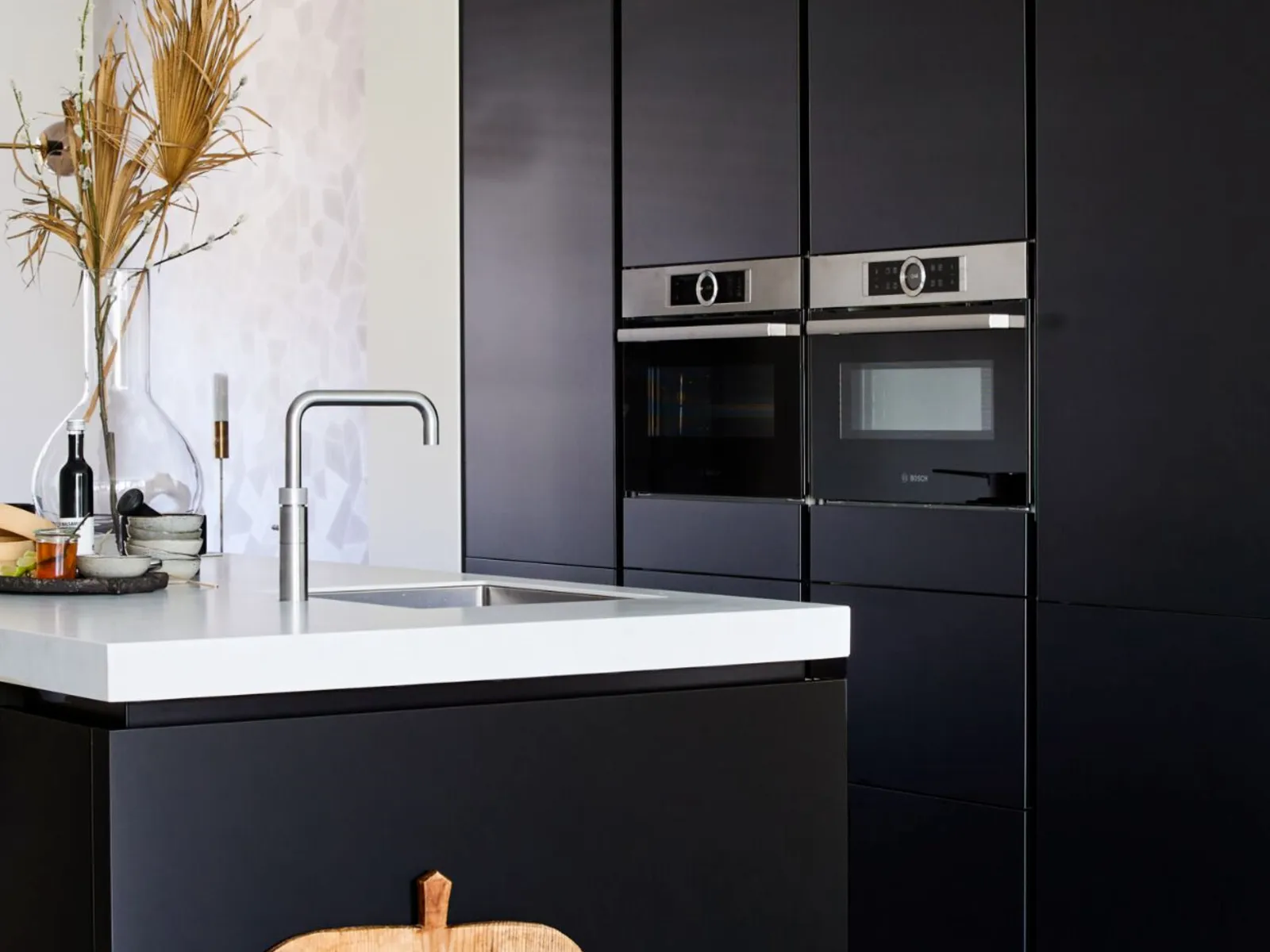 Cuisine moderne avec armoires noires, comptoir blanc et appareils en acier inoxydable.