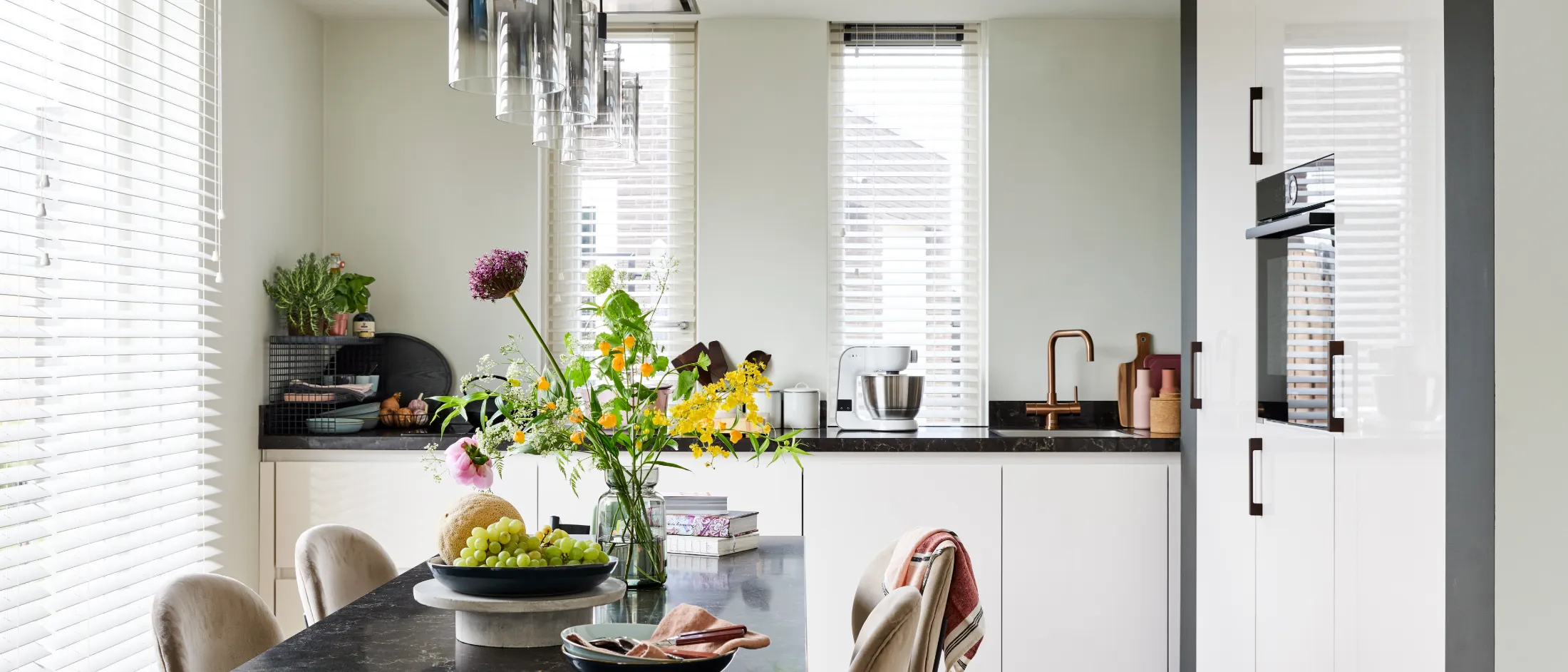Cuisine moderne avec table à manger, pendentif, plantes et décor minimaliste.