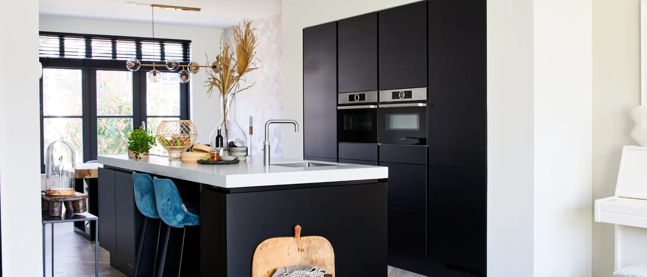 Cuisine moderne avec armoires noires, comptoirs blancs et éléments de décoration naturels.