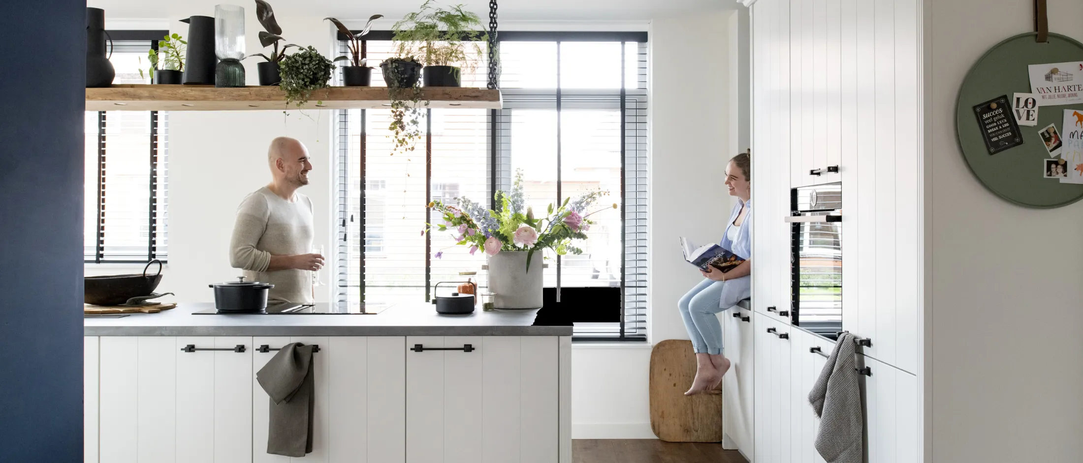 Cuisine moderne avec armoires blanches, plantes et personne debout au comptoir.