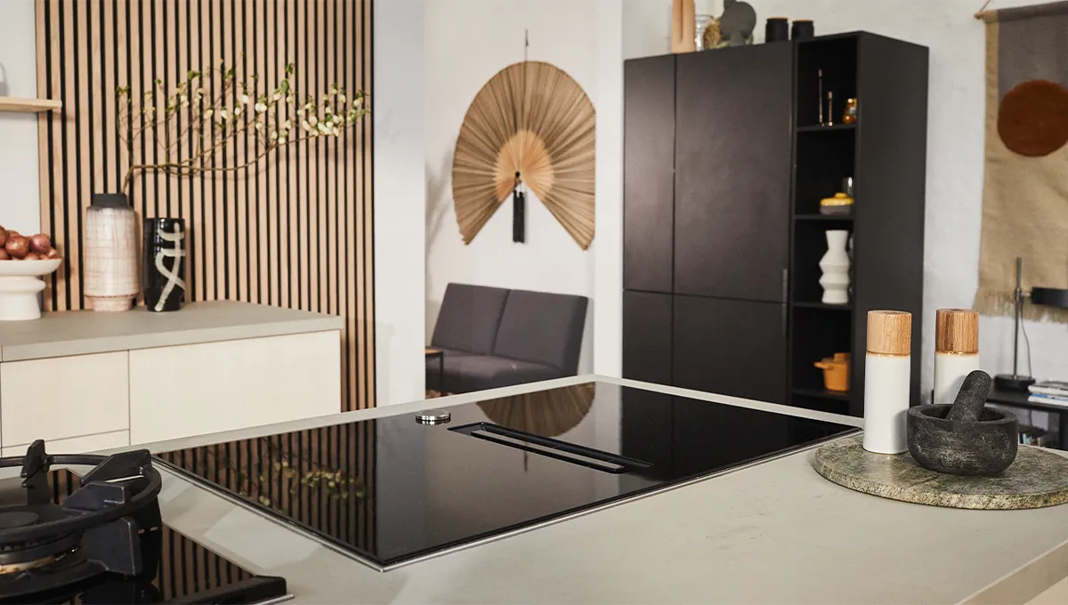 Un piano cottura a induzione ventilato NEFF è al centro di un'isola della cucina, con vista sulla zona giorno in stile Japandi e sui mobili neri sullo sfondo.