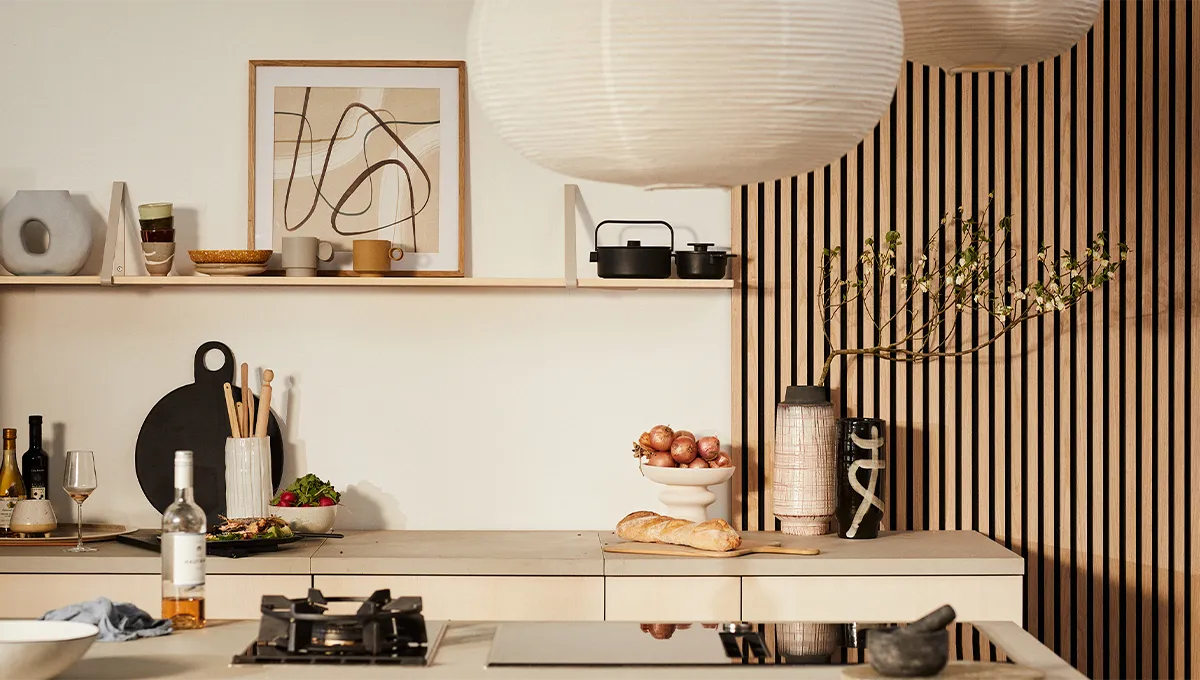 Un elegante bancone da cucina Japandi con un piano cottura domino NEFF, su uno sfondo di una parete a doghe di legno e una mensola aperta con arte e ceramiche.