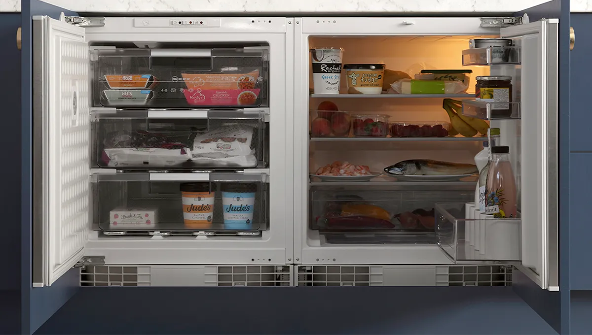 A front-on view of an open, side-by-side NEFF integrated fridge and freezer, revealing a neatly organized interior filled with fresh and frozen foods.