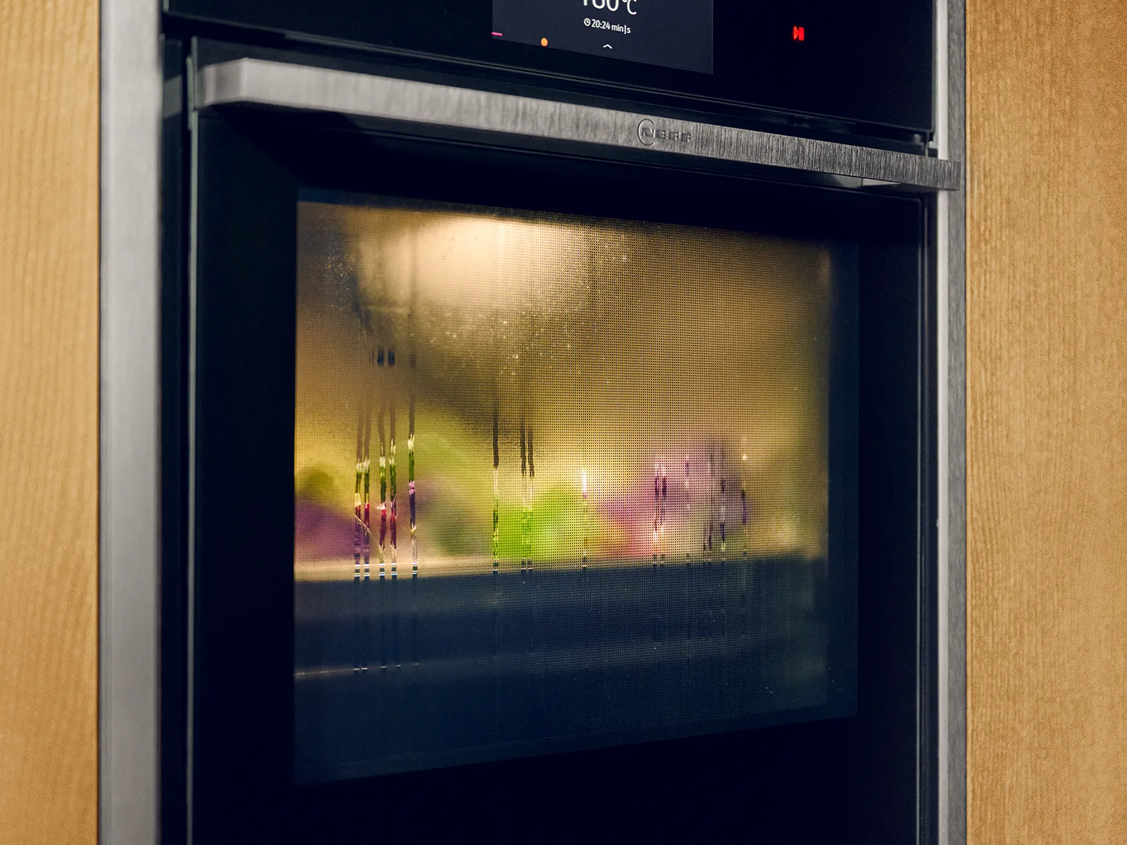 Ein Blick in den Innenraum des Backofens mit Kondenswasser an der Glasscheibe, verschwommenen Lichtern und der Temperaturanzeige im Hintergrund.