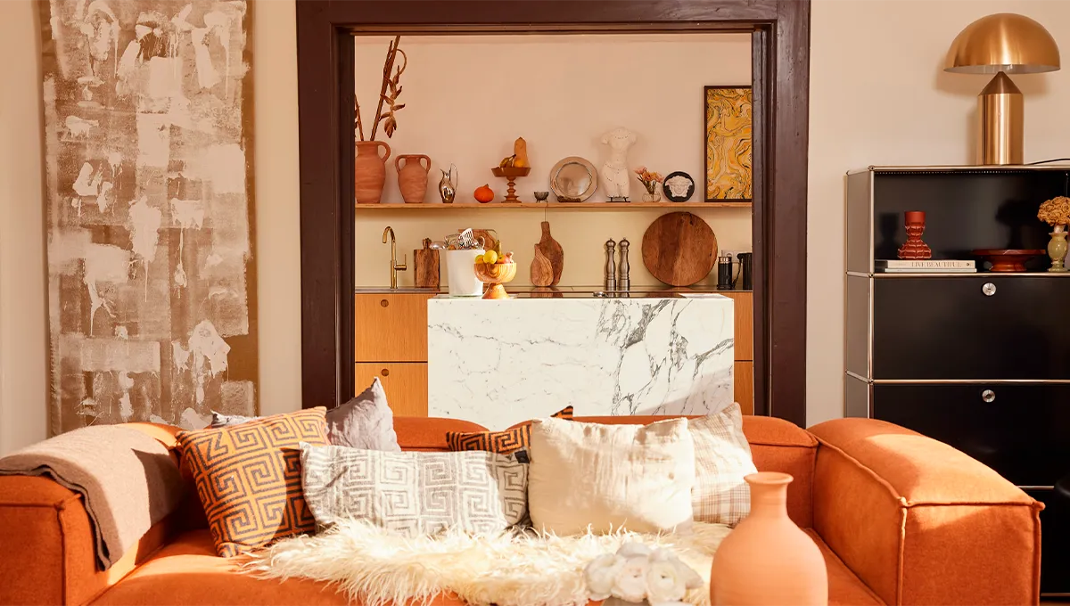 Cozy living room with orange sofa, shelves with decorative items, and a marble-topped cabinet.