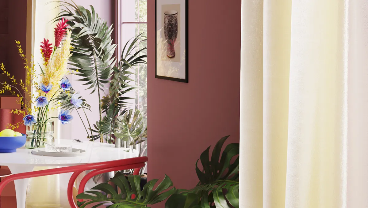 Ein kleiner weißer Tisch und ein roter Stuhl stehen vor einem großen Fenster; auf dem Tisch stehen bunte Blumen. An der roten Wand hängen zwei Bilder, und auf dem Boden befindet sich eine weitere Pflanze.