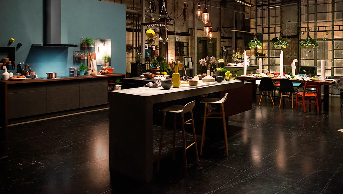 Küche im Industrial-Stil mit modernen Geräten, hängenden Pflanzen und einer langen Theke mit Barhockern.