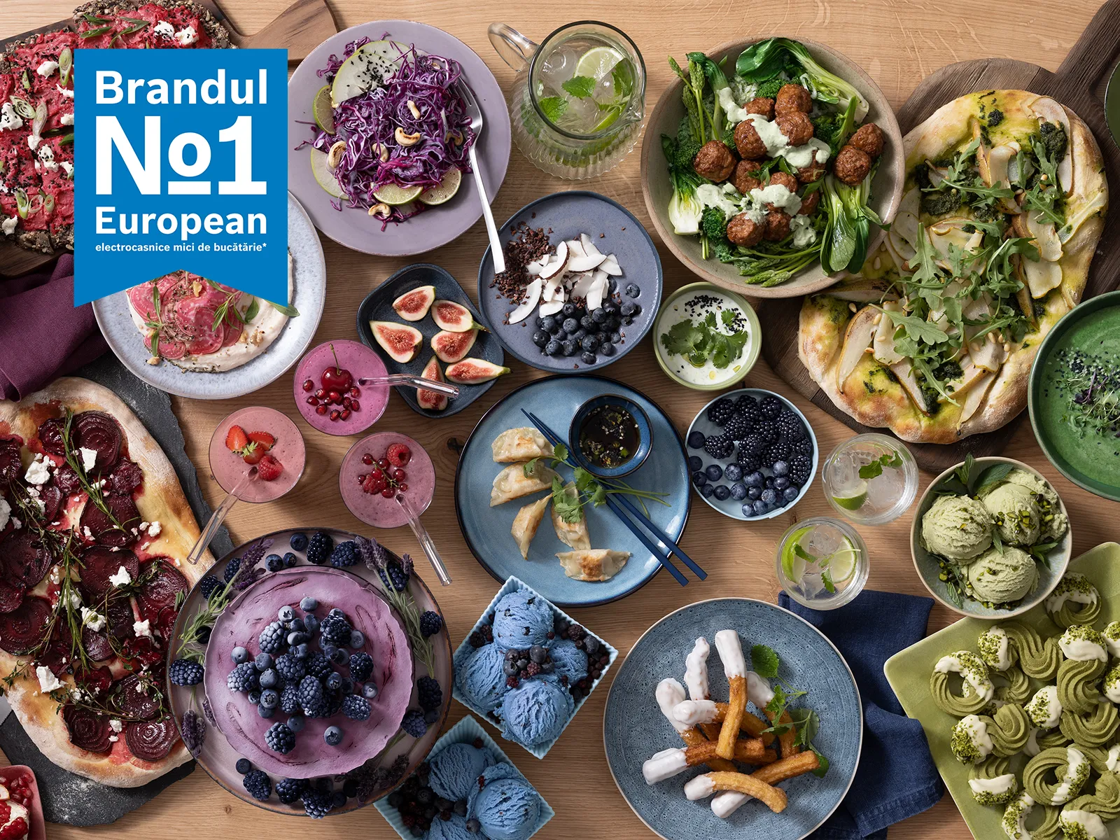 Brandul numărul 1 în Europa pentru aparate de preparare a alimentelor, expusă deasupra unei mese pline cu preparate, deserturi și băuturi vibrante.