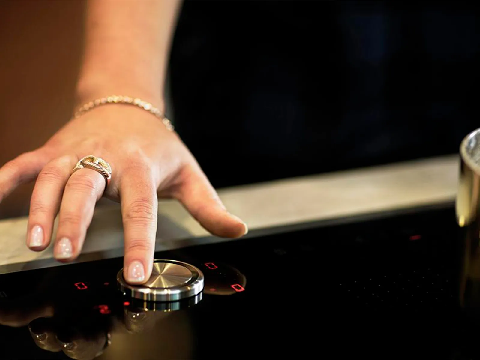 A close-up of a woman's hand using the magnetic Twist Pad® dial to control a black NEFF induction cooktop.