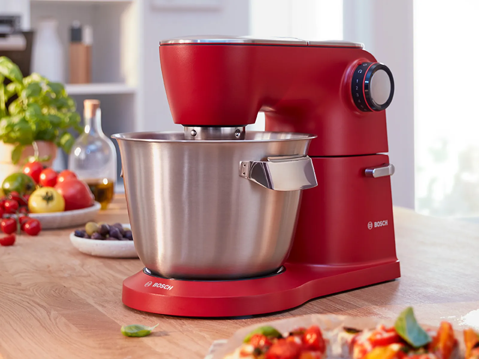 Rote Küchenmaschine auf der Küchentheke mit frischen Produkten und Pizzastücken.