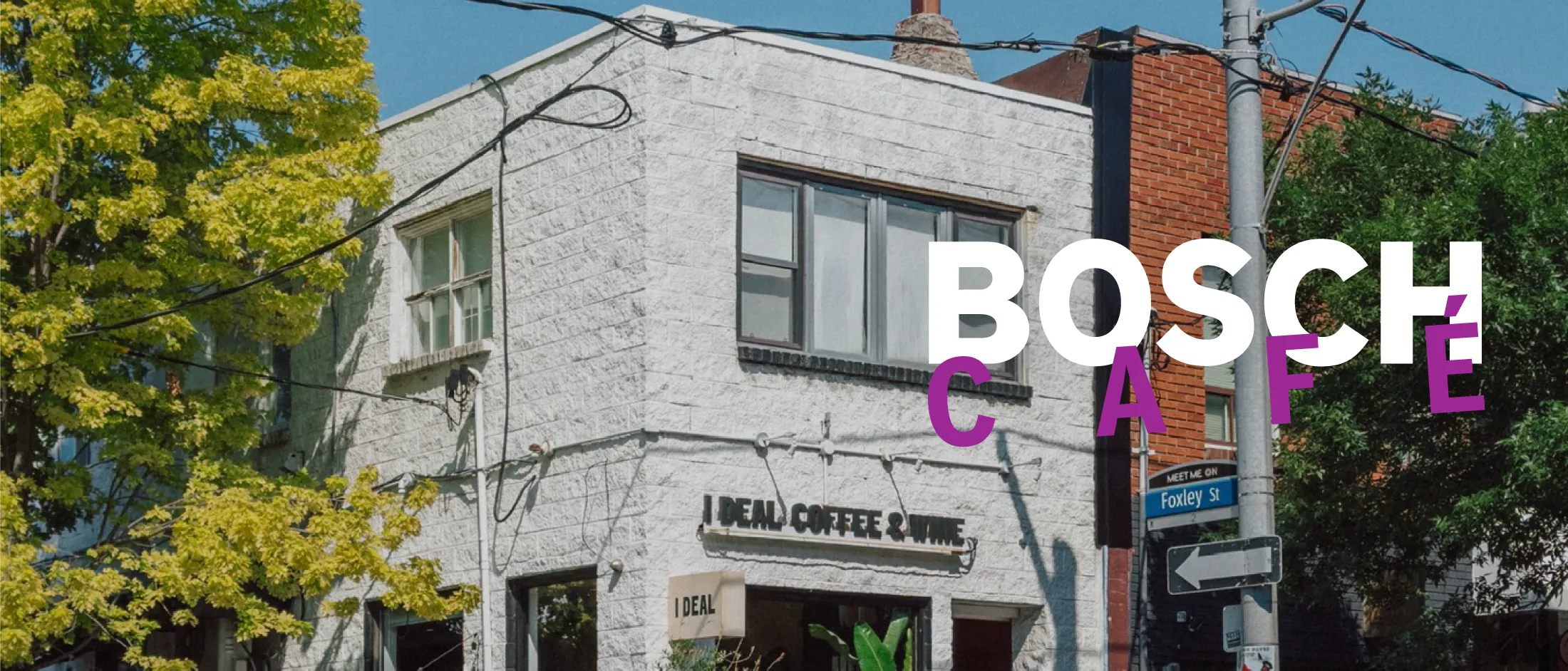 White brick corner café building with "IDEAL COFFEE & WINE" sign, street sign for Foxley St, and trees under a clear blue sky.