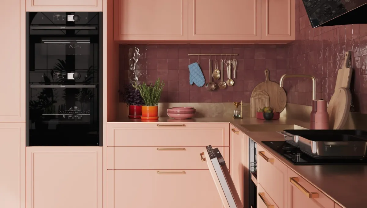 Eine moderne Küche ist mit pfirsichfarbenen Schränken, einem schwarzen NEFF-Backofen und einem Geschirrspüler ausgestattet; an der Wand hängen Küchenutensilien. Auf der Arbeitsplatte stehen eine Topfpflanze sowie Kochgeschirr.