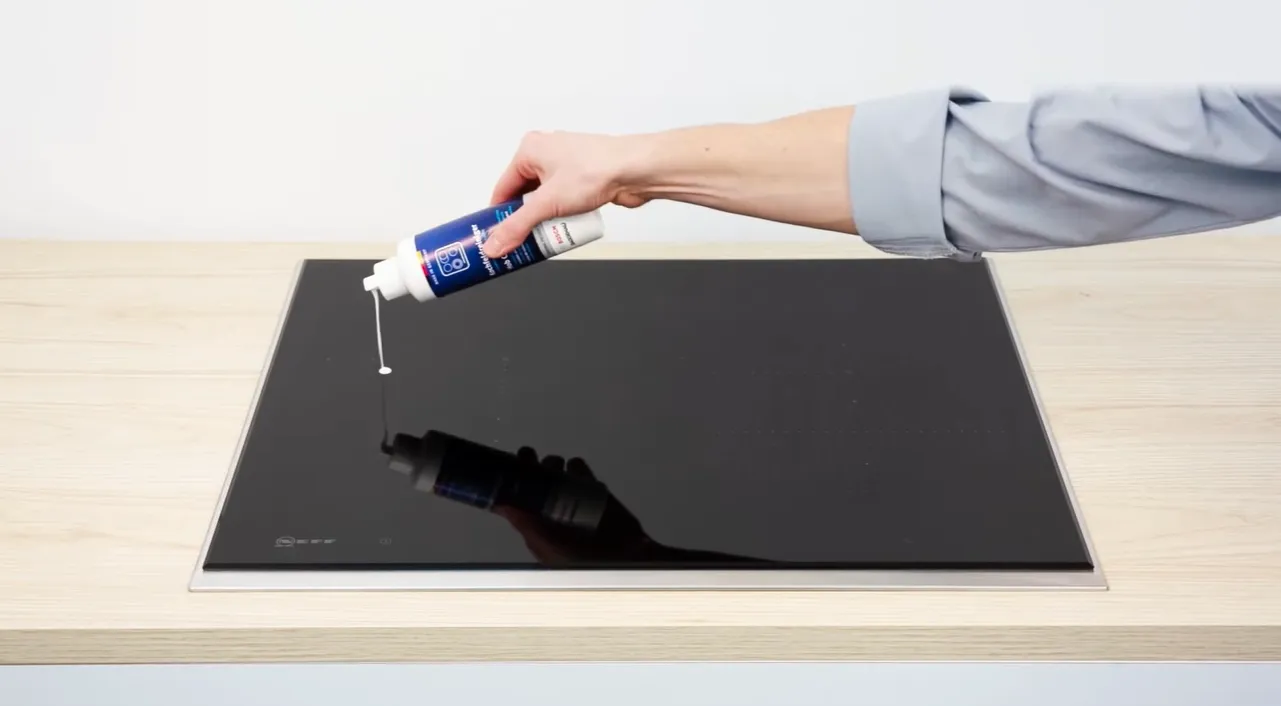 Person hand with a cleaning product spreading the liquid over the induction hob.