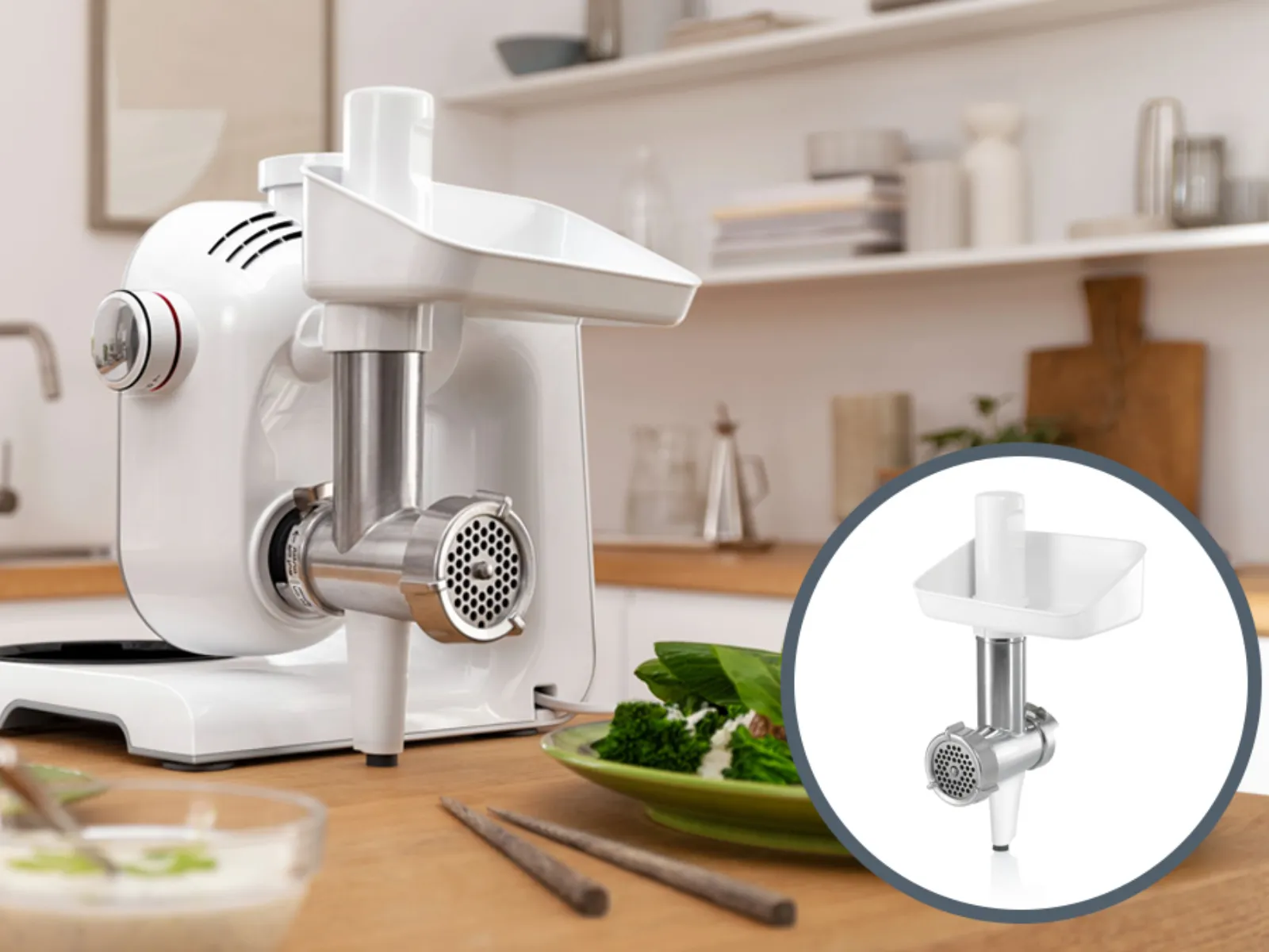 Electric meat grinder on kitchen counter with fresh ingredients, utensils, and shelves in background.