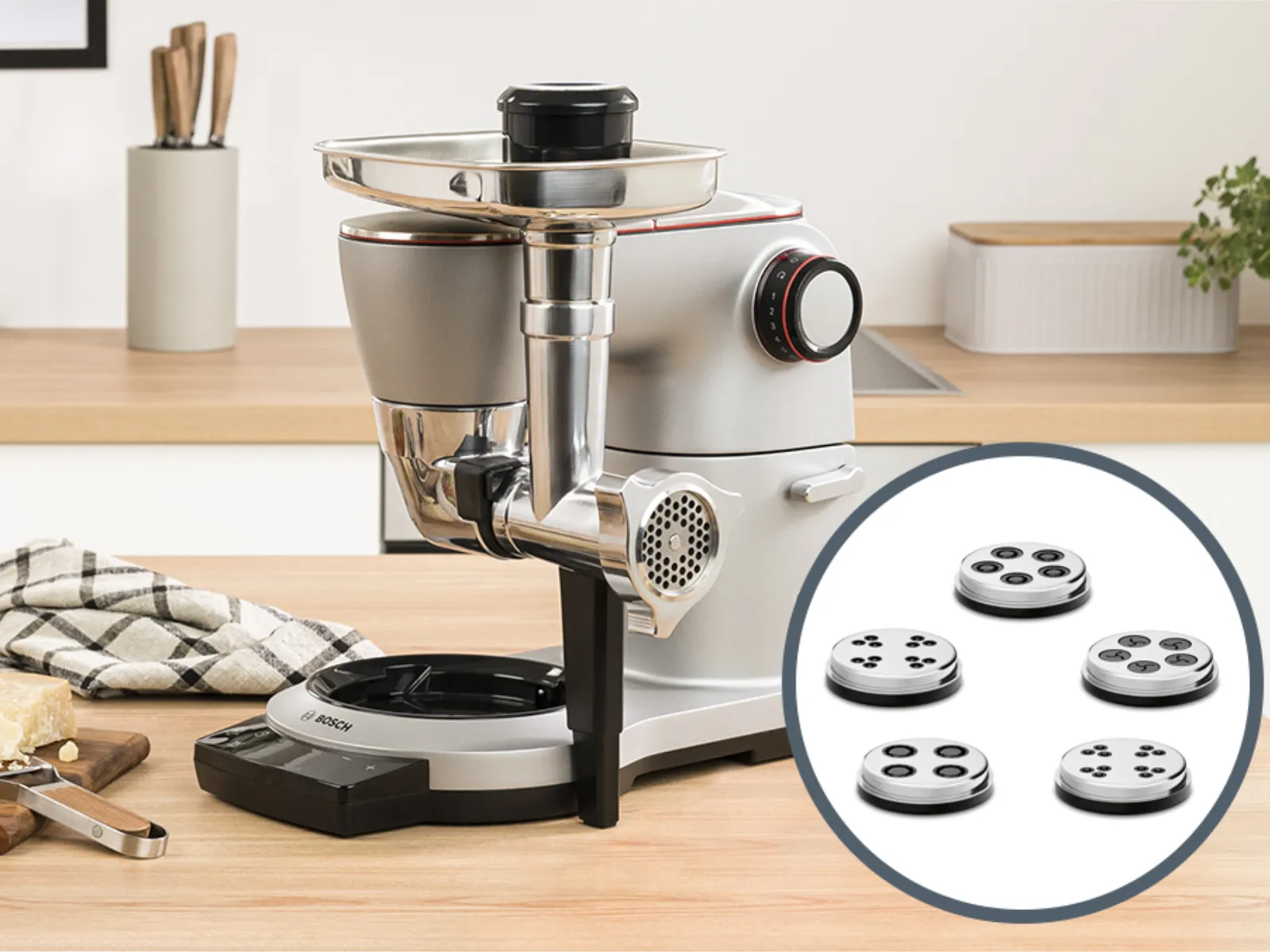 Kitchen counter with food prep tools, including a meat grinder, utensils, and a bowl of fresh produce.