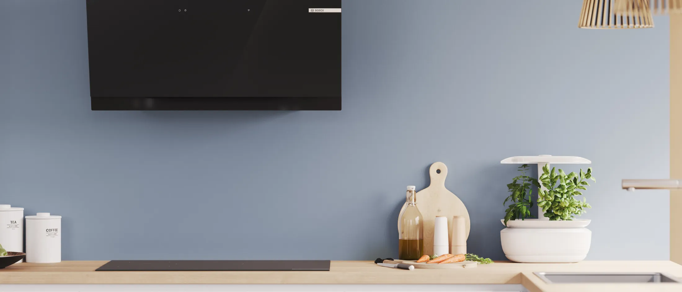 Modern kitchen countertop with a cutting board, bottle, herbs, carrots, and tea and coffee canisters against a blue wall.