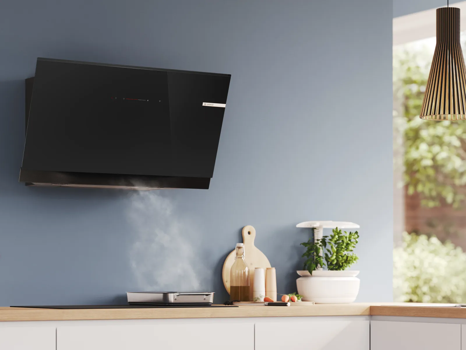 Modern kitchen with black range hood venting steam, light blue wall, wooden countertop, herbs, and utensils by a large window.