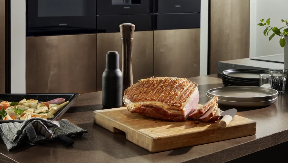 Porc rôti doré à la peau croustillante, tranché sur une planche à découper en bois dans une cuisine moderne.