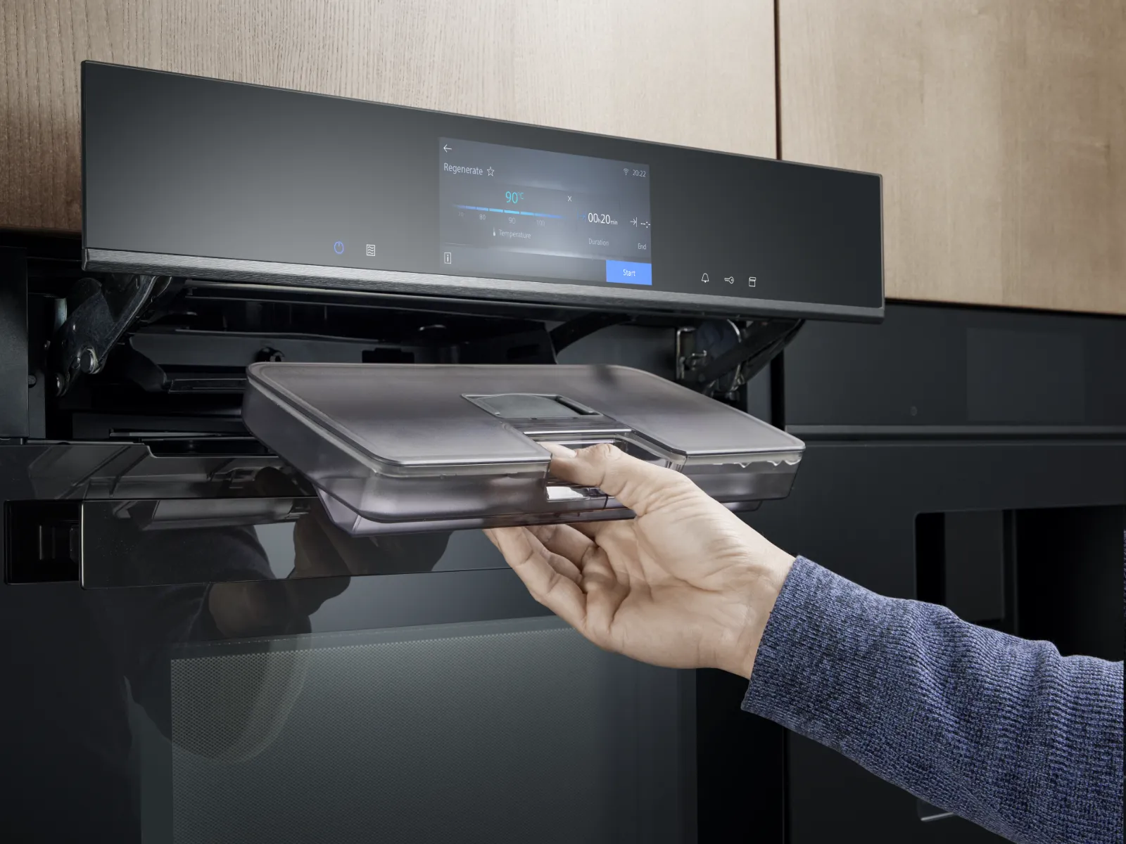 Een hand die een waterreservoir verwijdert uit een moderne inbouwoven met een digitaal display dat is ingesteld op 90 °C gedurende 20 minuten.