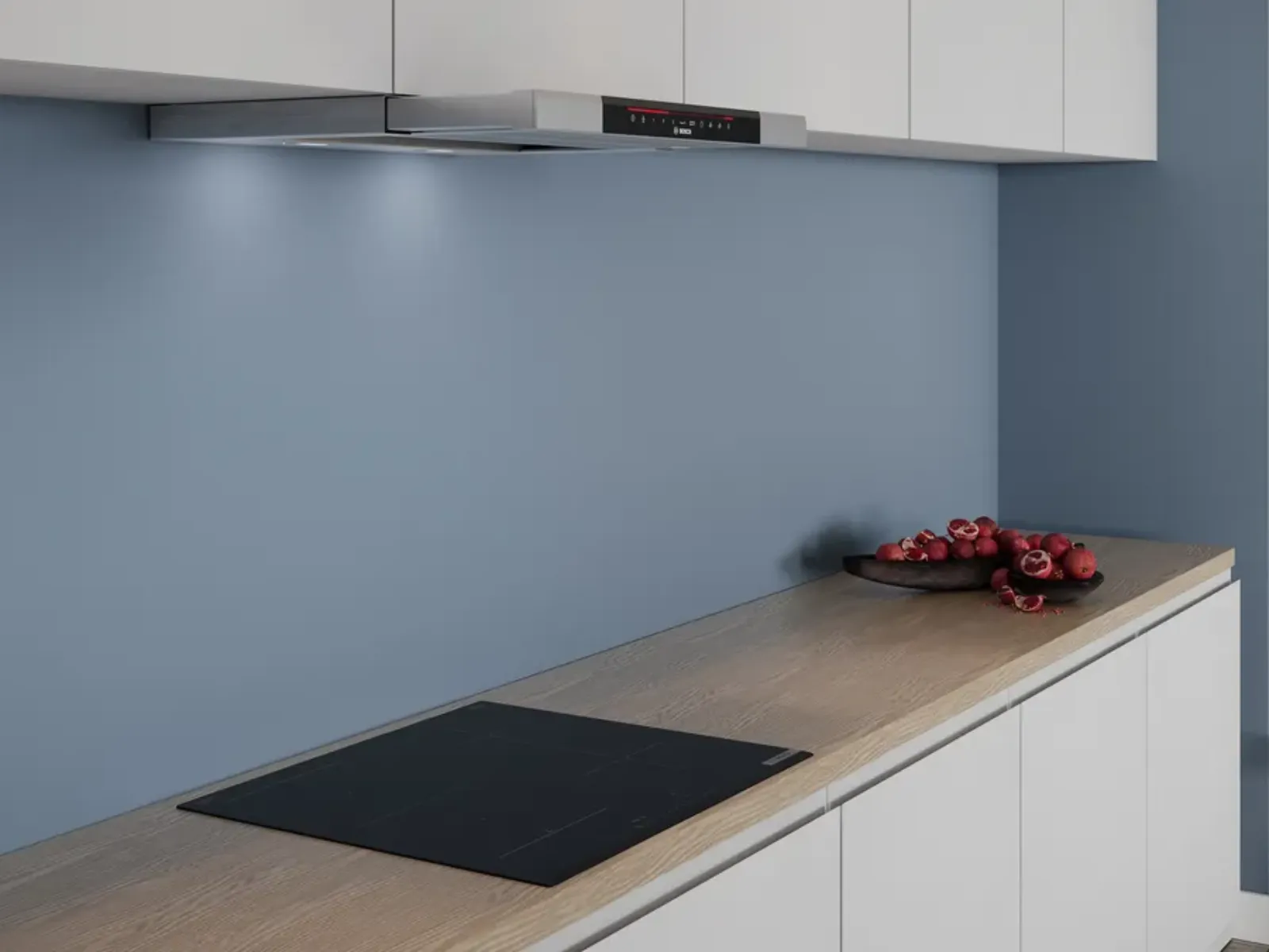 Modern kitchen countertop with built-in black induction cooktop and white cabinets under blue wall with overhead range hood and bowl of red onions