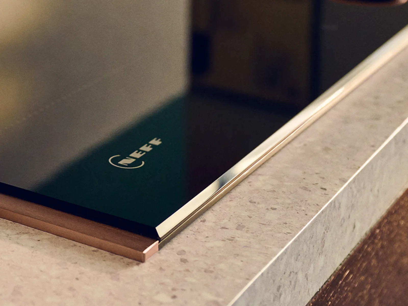 Close-up of a sleek Neff black induction cooktop embedded in a beige speckled kitchen countertop.