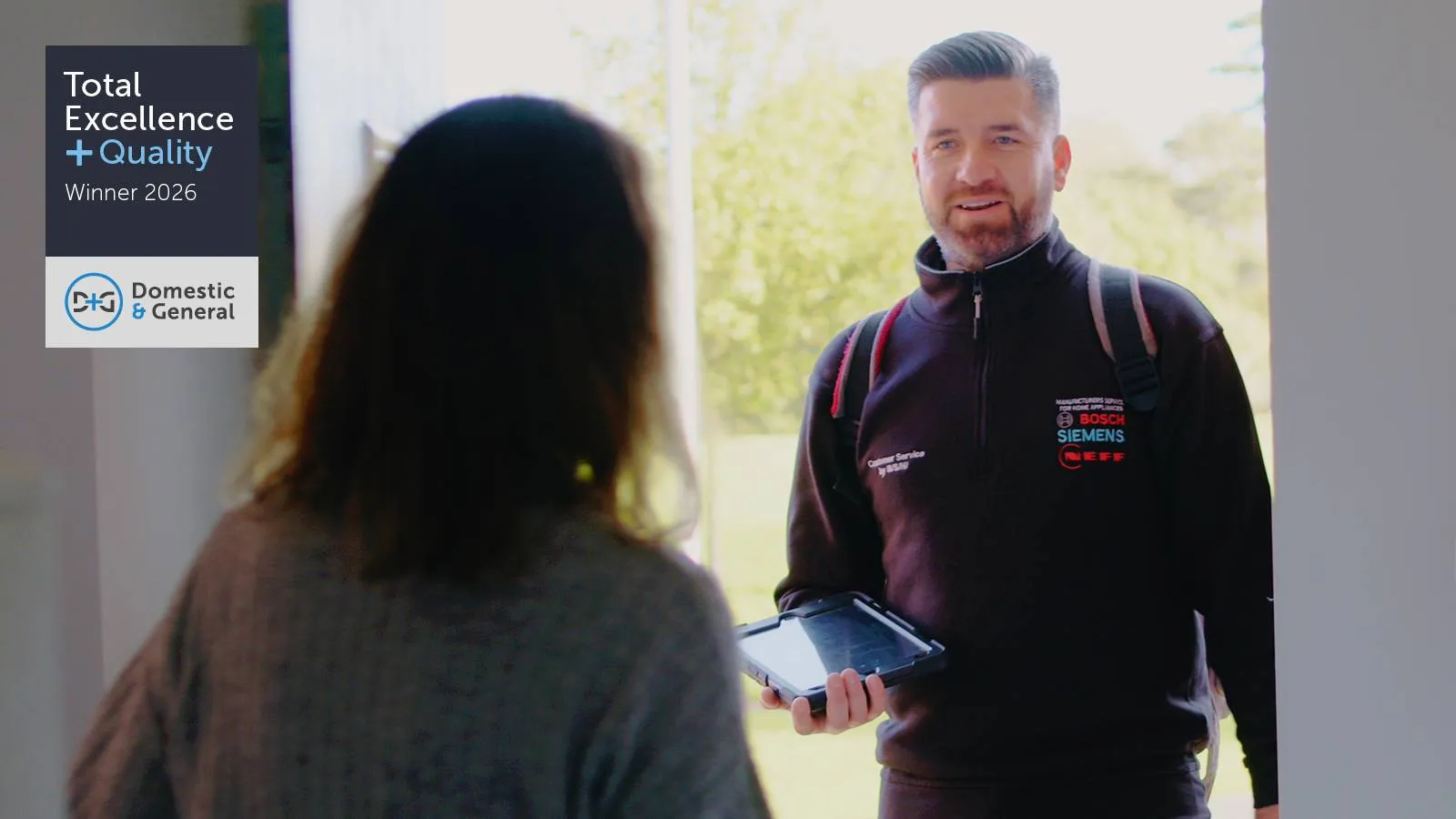 A person with an electronic tablet at the door of another person with the "Total Excellence + Quality" award displayed
