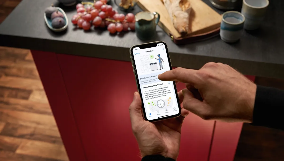 Person using smartphone to access online banking app on kitchen counter with grapes and bread.