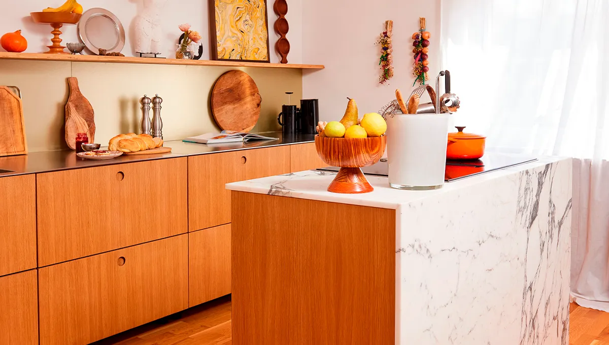 A bright, modern kitchen featuring light wood cabinets and a striking white marble island with an integrated cooktop.